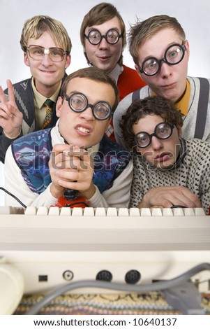 Five nerdy guys sitting in front of old-fashioned keyboard. They are looking at camera. One of them is holding joystick. Front view