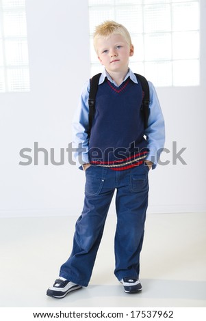 Young schoolboy standing with backpak. He's keeping hands in pocket. He's looking at camera. Front view.