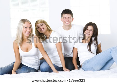Group of young smiling friends sitting on bed and looking at camera.  Front view.