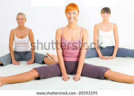 Group of women sitting on the floor and doing fitness exercise. They\'re looking at camera. Front view.