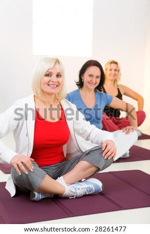 Elder women sitting cross-legged on mat and doing exercices. They\'re smiling and looking at camera.