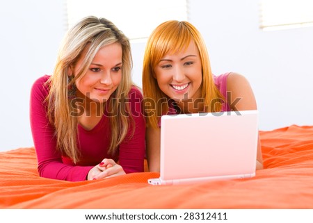 Young women lying on bed and doing something on laptop. Front view.