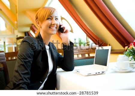 Young woman sitting in restaurant and speaking by cellphone.