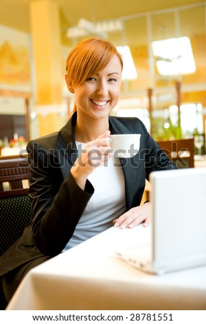 Young woman with laptop sitting in restaurant. She\'s drinking coffee.