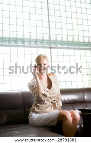 Blonde woman sitting on couch and speaking by cellphone.