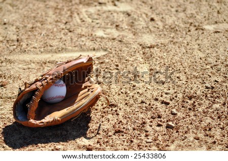 Baseball and glove on dirt infield with copy space.