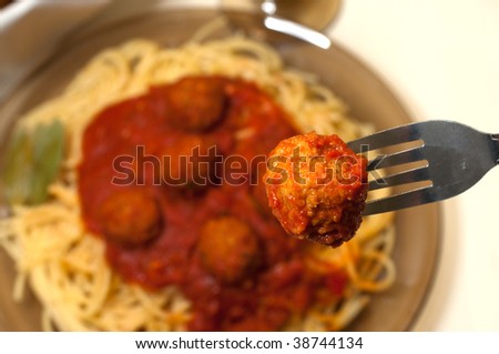 Spaghetti and meatballs with closeup of meatball on fork.
