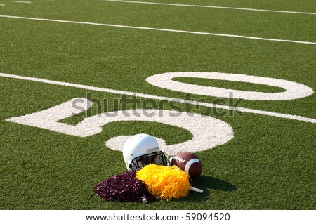 American football, helmet, and pom poms on field next to 50 yard line.