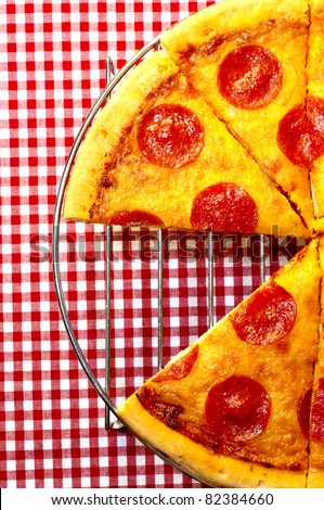 Pepperoni pizza half with slice removed on red gingham tablecloth.