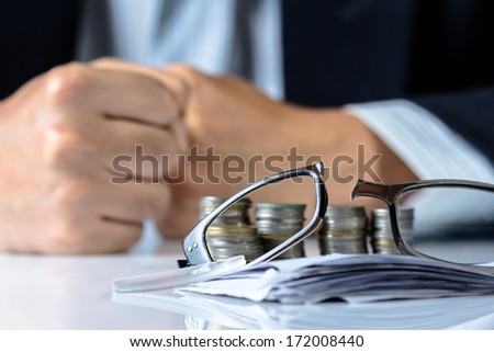 Broken eyeglasses on financial desk with fist of businessman, losing money or business ruined concept