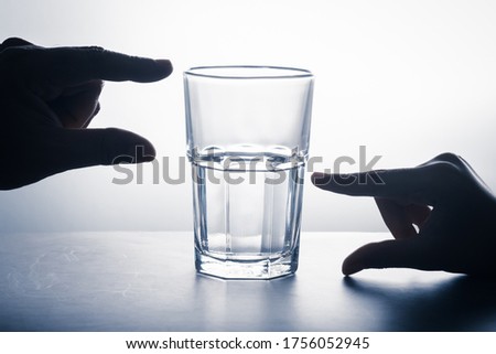 Hands measure on glass that has an empty part and left water, glass half full attitude concept, crisis and opportunity point of view