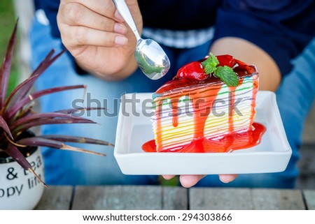 Rainbow crape cake on white plate with woman\'s hand going to eat