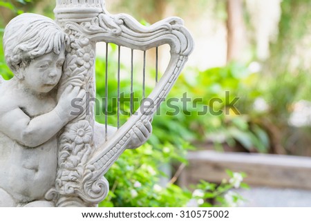 Old Cupid statue playing harp, decorated in the garden