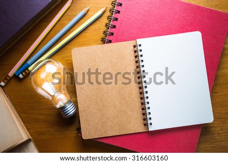 Opened spiral notebook with glowing light bulb on wood table