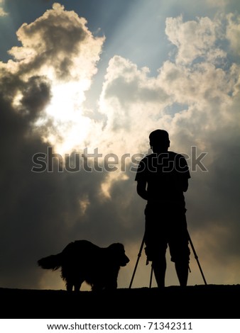 Photographer with his dog on the top of the mountain in silhouette