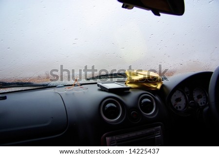 The dashboard on a very rainy day in the Australian outback, featuring a pair of spectacles, GPS unit and a gold cosmetic case.