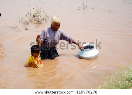 GUJRANWALA, PAKISTAN - AUG 24: Flood affected woman with her child pass through flood water at a flood hit area in Mianwali Hafizabad District on August 24, 2012 in Gujranwala, Pakistan.