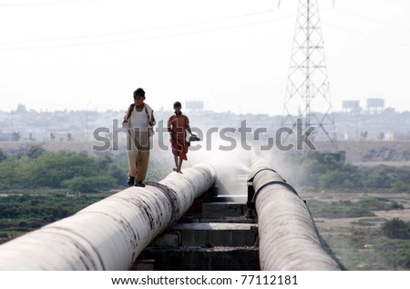 KARACHI, PAKISTAN - MAY 12: Two children pass over a broken drinking water pipeline at Korangi crossing which needs the attention of Water and Sewerage Board (KWSB) on May 12, 2011 in Karachi, Pakistan.