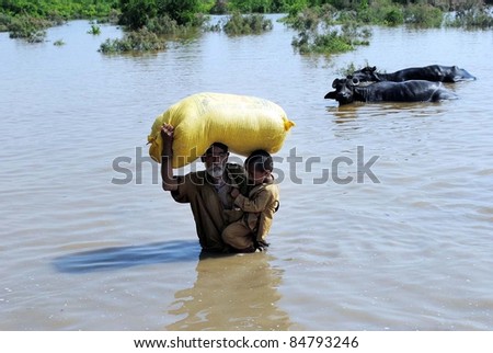 HYDERABAD, PAKISTAN - SEPT 16: An aged rain affected man holds a child and bag over his head passes through a flooded area as he is moving towards safe place after his house was inundated with rainwater September 16,2011, Hyderabad