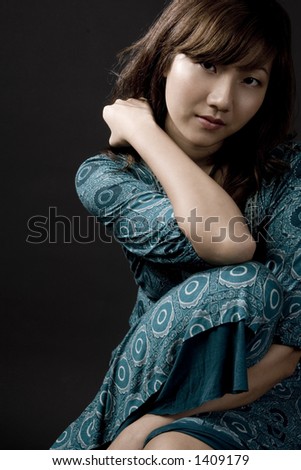 A beautiful young asian woman in a seated pose on black background