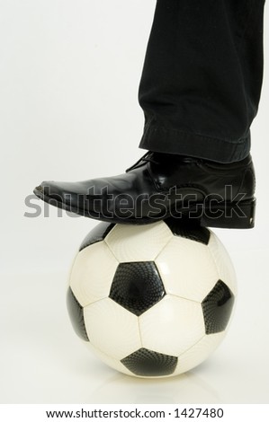 A leg and smart shoe stepping on a football (soccer ball)