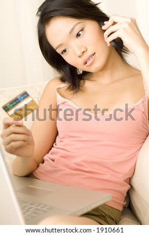 An attractive young asian woman sitting on couch at home with laptop computer, mobile phone and credit card (shallow depth of field used)