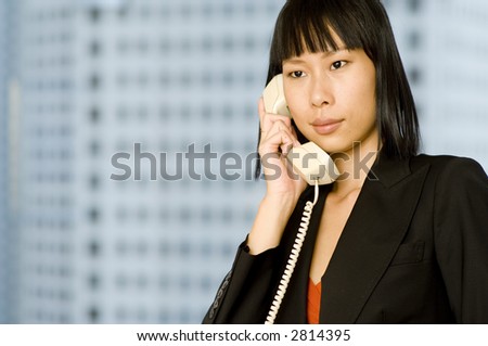 An attractive chinese businesswoman holding phone with office building out of focus behind