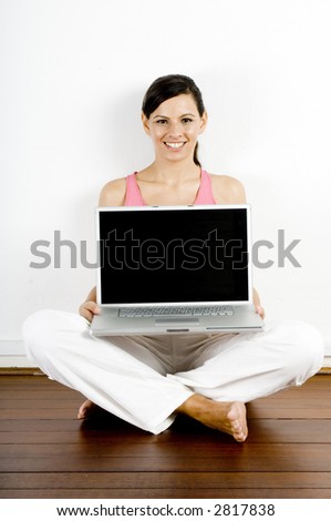 A young woman sitting on the floor holding a laptop computer with screen facing camera
