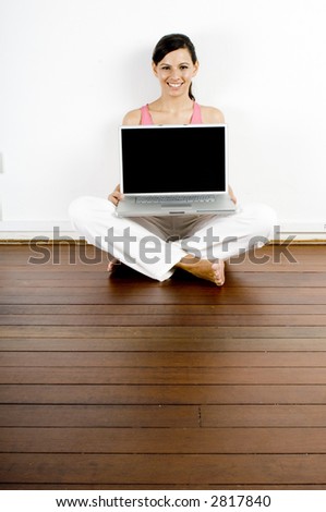 A young woman sitting on the studio floor holding a laptop computer