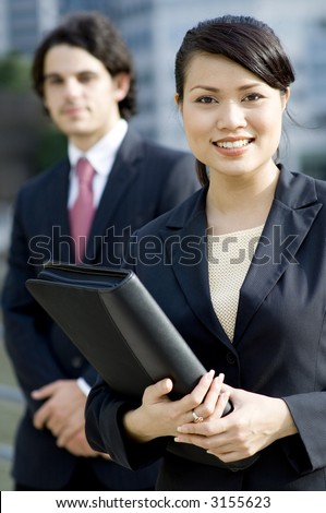 A young businesswoman standing outside with a male colleague standing behind her (shallow depth of field)