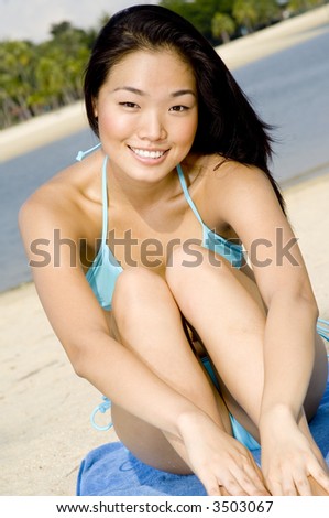 A young attractive Asian woman in blue bikini sitting on tropical beach