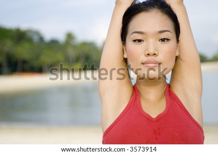 A young attractive Asian woman stretching arms above her head on a tropical beach