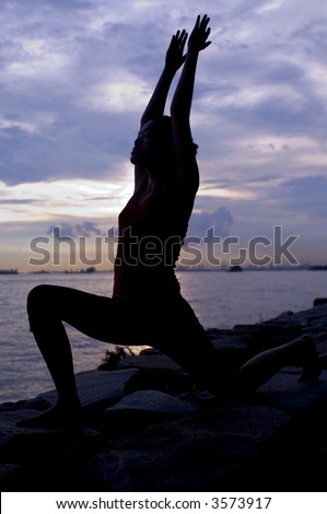 A young woman doing a yoga warrior pose by the ocean