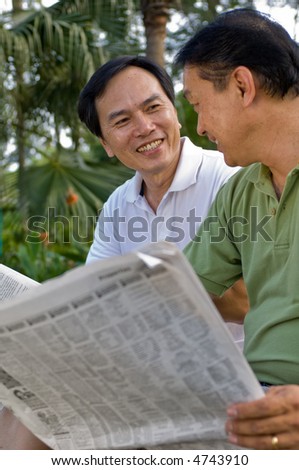 Two Chinese men in their fifties reading the newspaper in the park