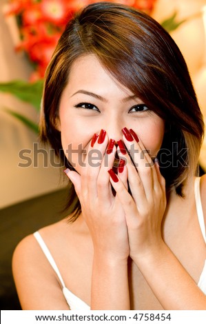 A young pretty asian woman laughing behind new red nails