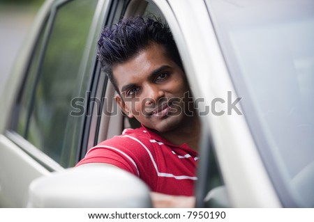 A handsome Indian man in a saloon car outside in countryside