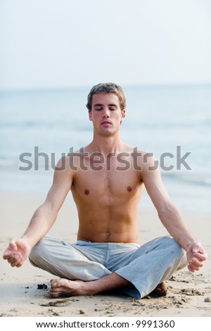 A young man in a relaxed sitting position on the beach with ocean behind