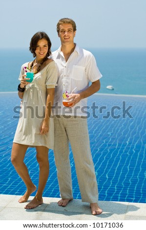 A stylish young couple with cocktails by the pool