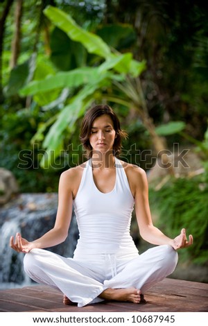 A young woman sitting outside in a yoga position looking very peaceful
