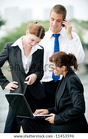 Three business executives with laptop outside by a river in the City
