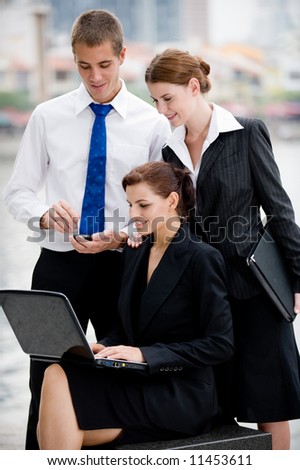 Three business executives with laptop outside by a river in the City