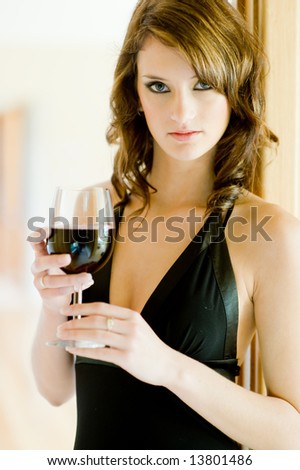 A beautiful young woman in black dress holding glass of red wine