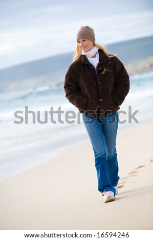A young attractive woman walking along a sandy beach in autumn