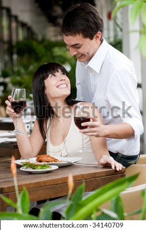 A young and attractive woman is surprised by her partner while dining in an outdoor restaurant