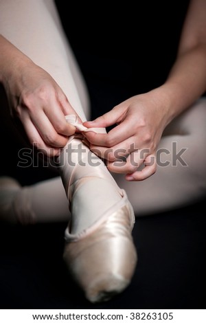 Close up of a ballerina tying her ballet shoes against black background