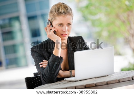 A businesswoman talking on her phone while using her laptop at an outdoor cafeteria