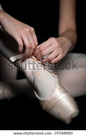 A ballerina tying her ballet slippers on, against black background