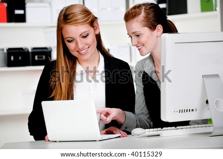 Two attractive businesswomen discussing work in front of a computer and a laptop in the office