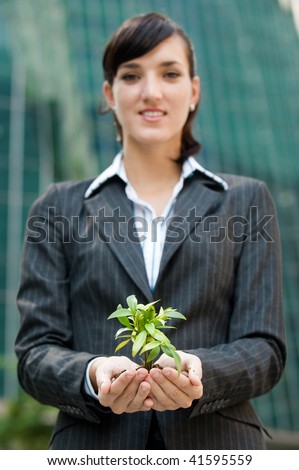 An attractive businesswoman cupping a plant in her hands against city backdrop