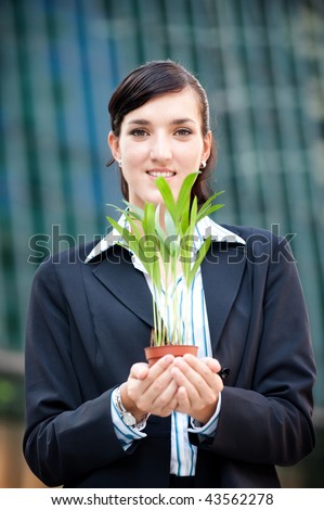 An attractive businesswoman cupping a plant in her hands against city backdrop